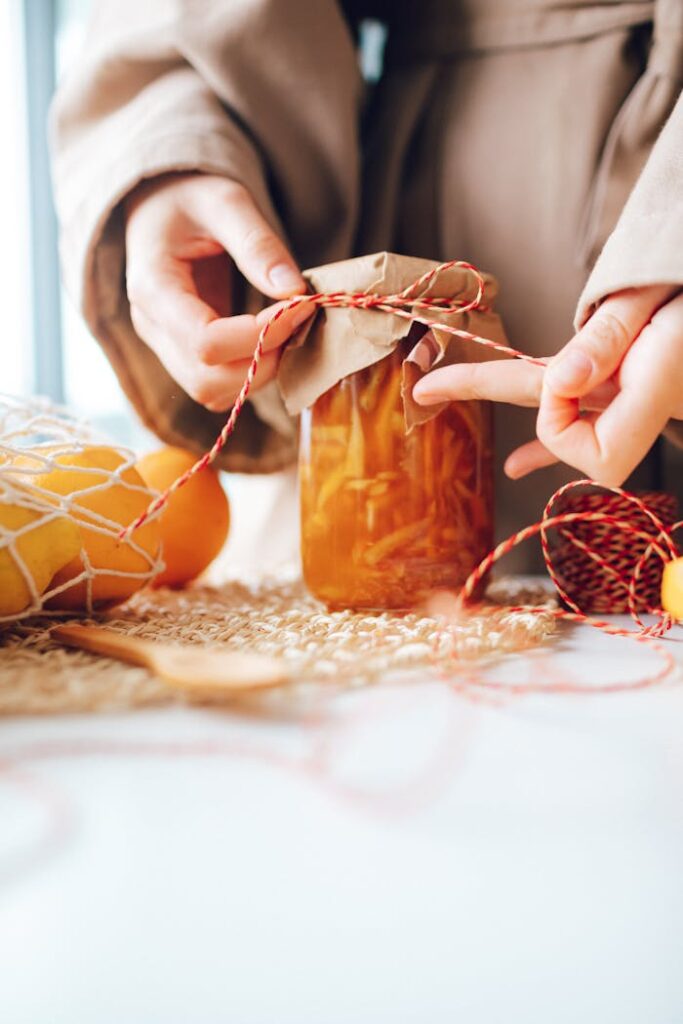 Hands wrapping a glass jar of homemade jam with rustic twine and paper.